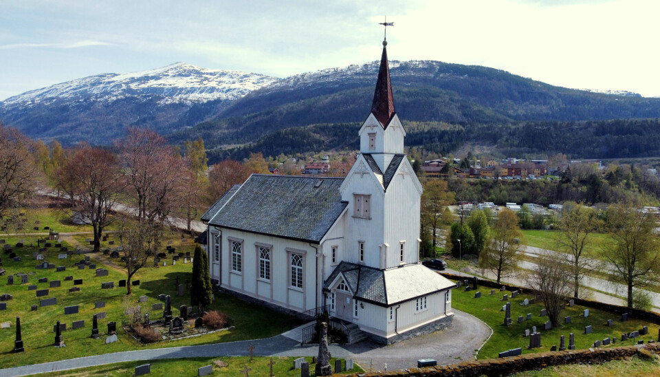 En hvit kirke i tre med fjell i bakgrunnen og grønt gress