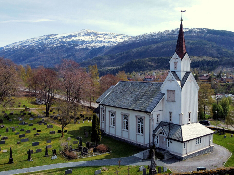 Gudsteneste i Øye kyrkje En hvit kirke i tre med fjell i bakgrunnen og grønt gress