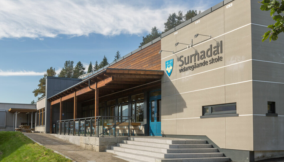 Et stort murbygg med trapper og asfaltert gangvei foran. På veggen Møre og Romsdal fylkeskommune sin logo og 'Surnadal vidaregående skole'