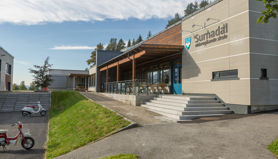 Et stort murbygg med trapper og asfaltert gangvei foran. På veggen Møre og Romsdal fylkeskommune sin logo og 'Surnadal vidaregående skole'