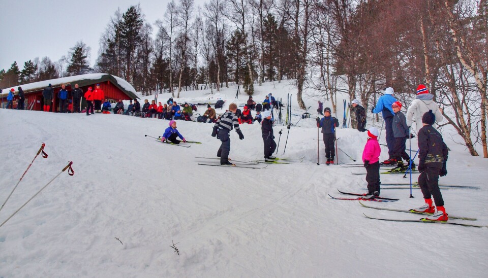 Flere barn som går og leker på ski. Mange mennekser og ei hytte i bakgrunnen.