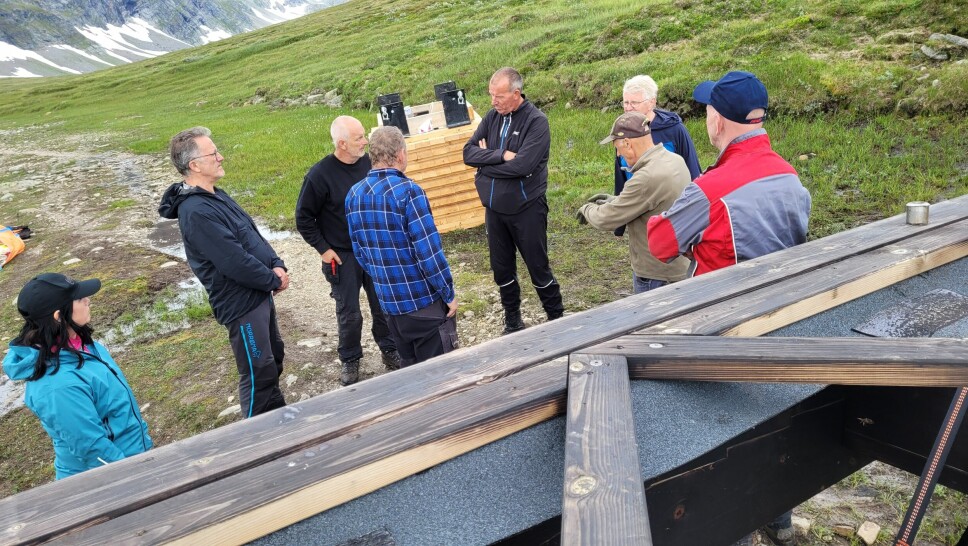 Per Gunnar Østerås, i helsvart antrekk midt i bildet, i dialog med sine frivillige hjelpere og leverandøren av brua Rennebu-bjelken.