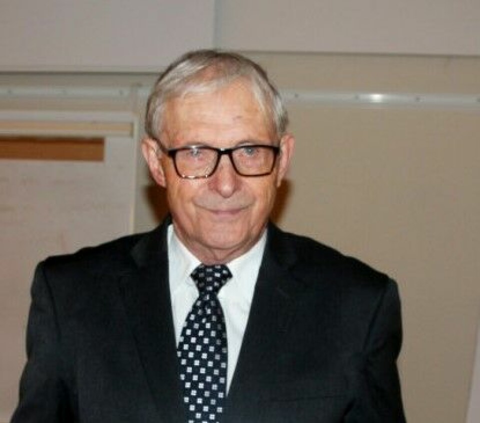 Portrettbilde av en eldre mann med grått hår, briller og svart dress