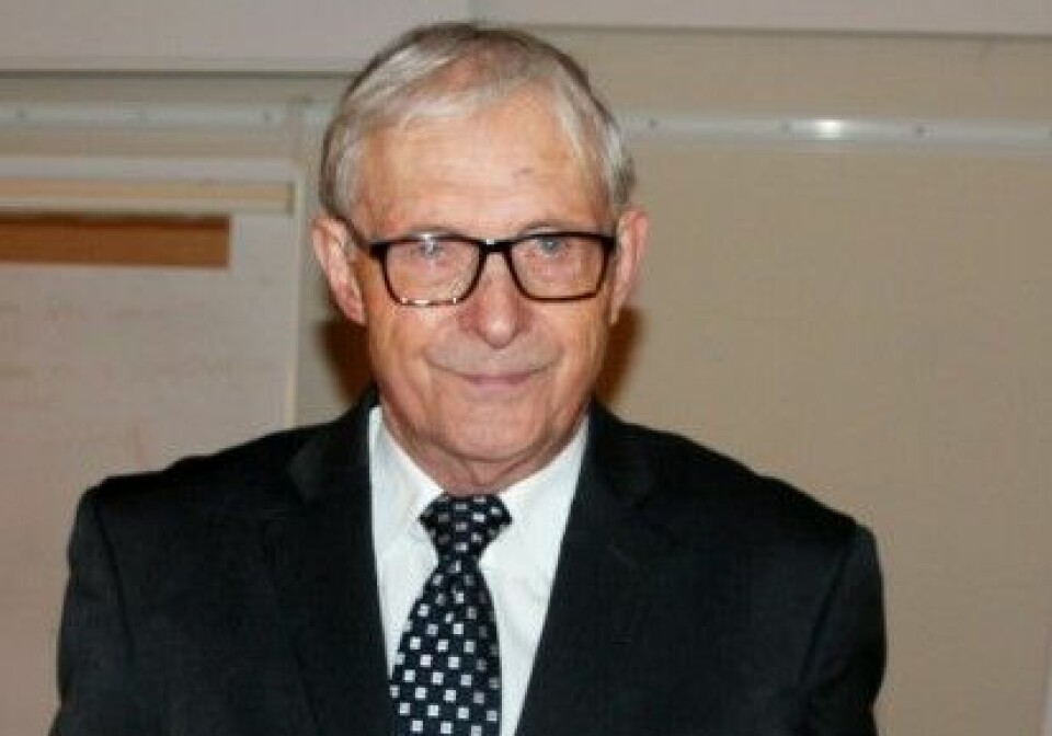 Portrettbilde av en eldre mann med grått hår, briller og svart dress