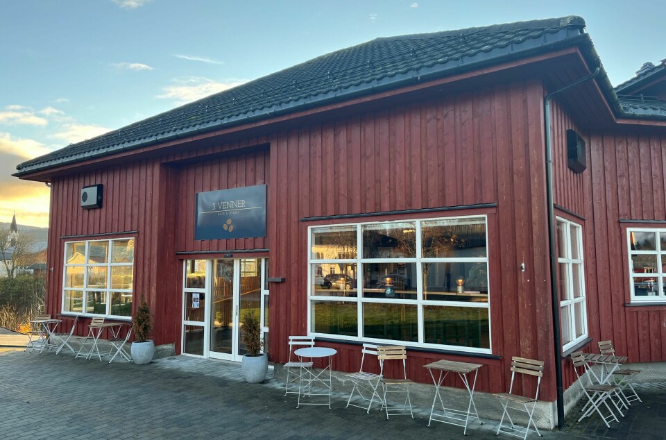 En rødmalt bygning med bord og stoler utenfor. Skilt med navnet og logoen til 3 Venner på veggen. Lokalene til kafeen 3 Venner i Rindal sentrum.