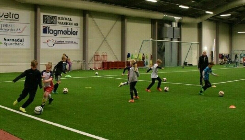 Flere barn som sparker fotball på en innendørs fotballbane, i Rindalshallen.