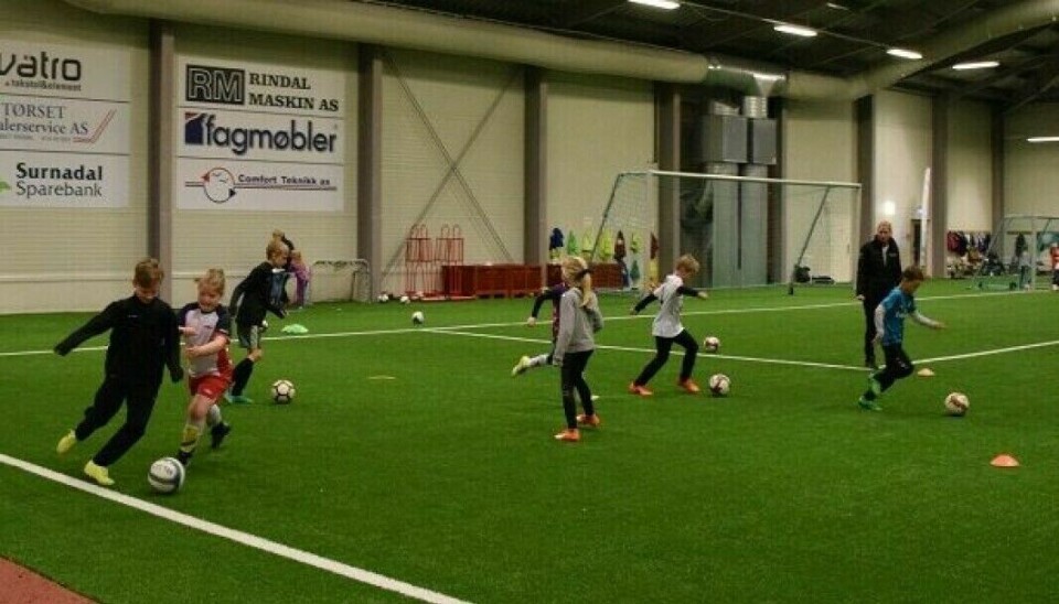 Flere barn som sparker fotball på en innendørs fotballbane, i Rindalshallen.