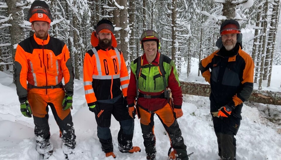 Fire smilende menn i verneutsyr i snøen i skogen.