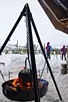 Kaffekjelen henger over flammene i bålpanna. Skiløpere på vei hjem i bakgrunnen.