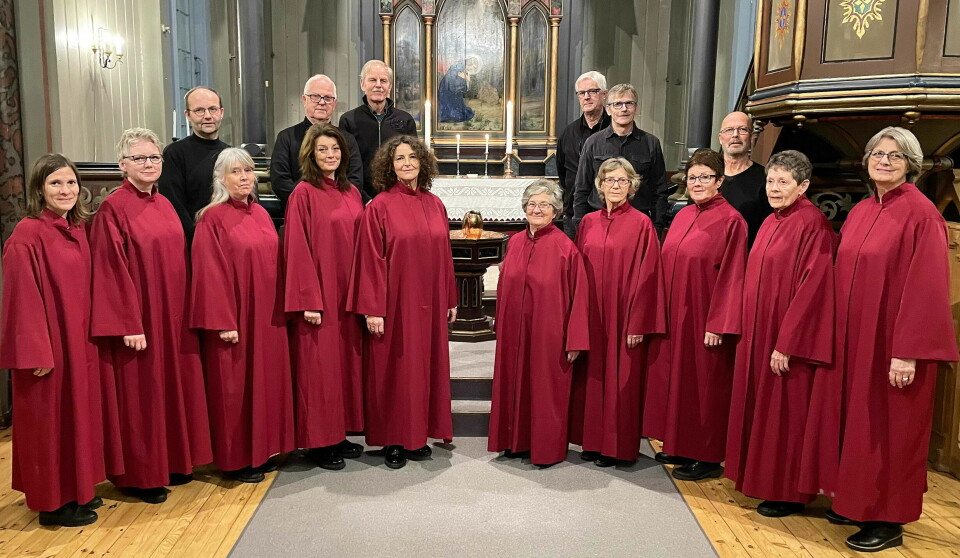 Seks menn kledd i svart står bak ti kvinner kledd i rødt fra koret.