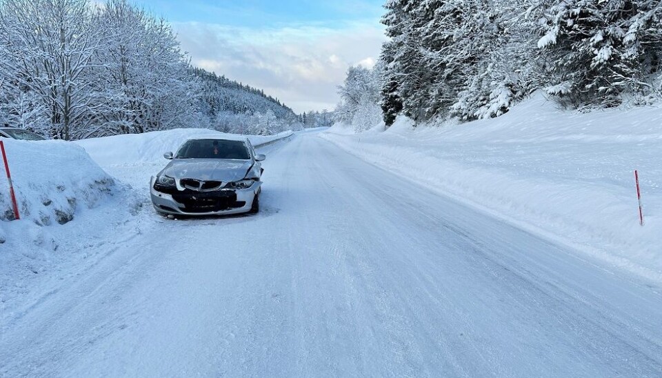 En lys grå bil som står i vegkanten på en snødekt vei, med skader i fronten etter å å kjørt i autovernet.