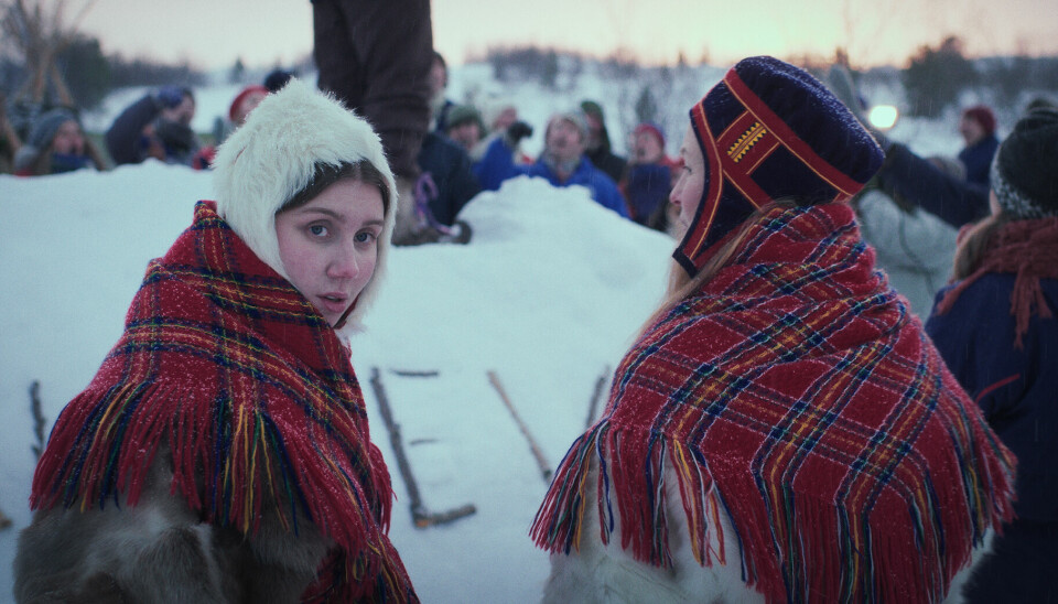 To kvinner kledd i reinskinn og rød rutete sjal i snøen i Nord-Norge.