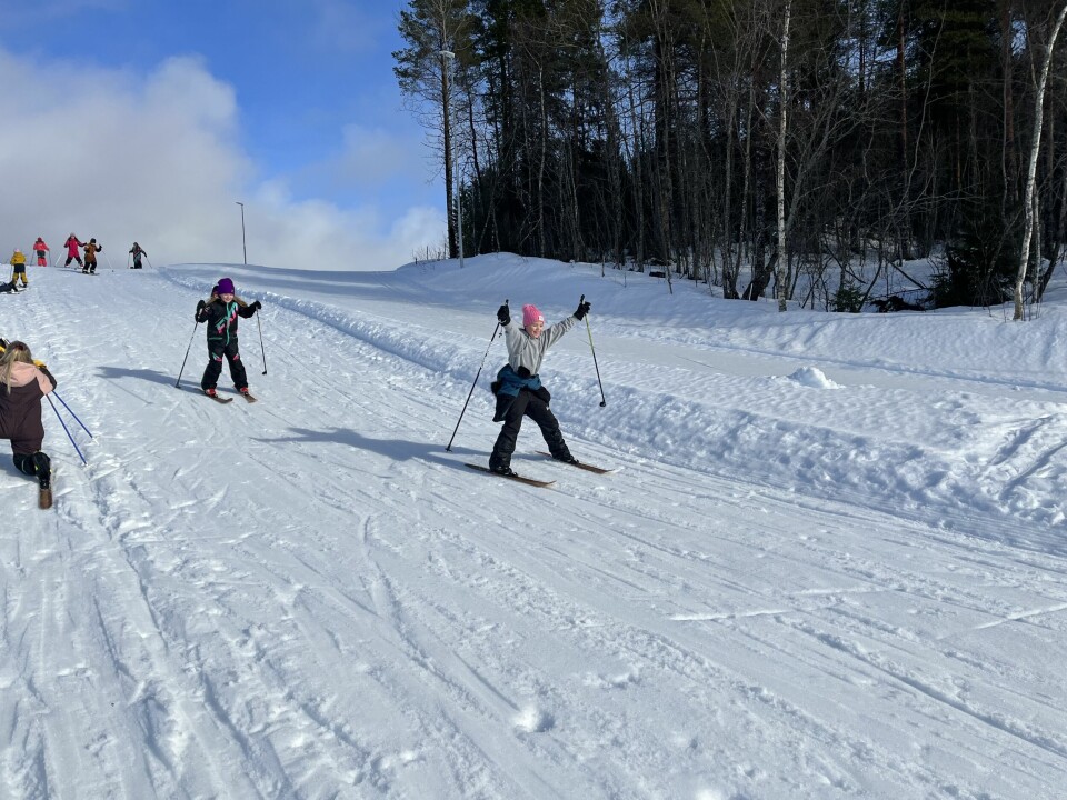 Flere barn som renner på ski nedover en bakke i ei preparert skiløype.