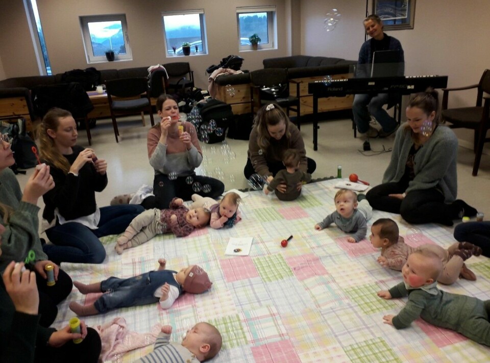 Flere babyer som ligger i ring på et teppe på gulvet. Mødrene sitter ved siden av.