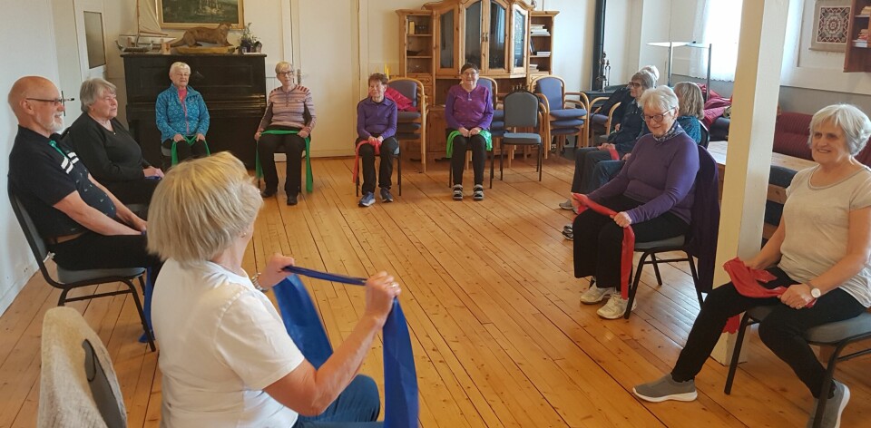 Pensjonister sitter på stoler og trimmer kroppene sine med strikk.