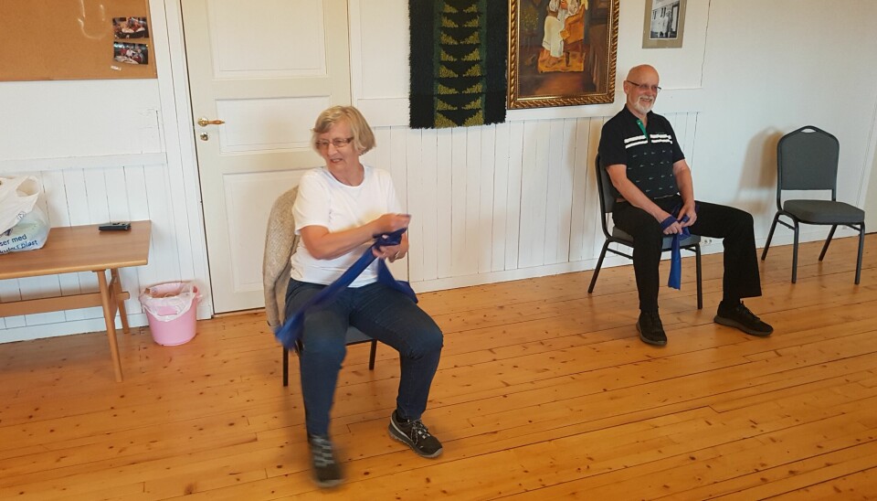 En kvinne og en eldre mann sitter med hver sin blåe strikk og strekker.