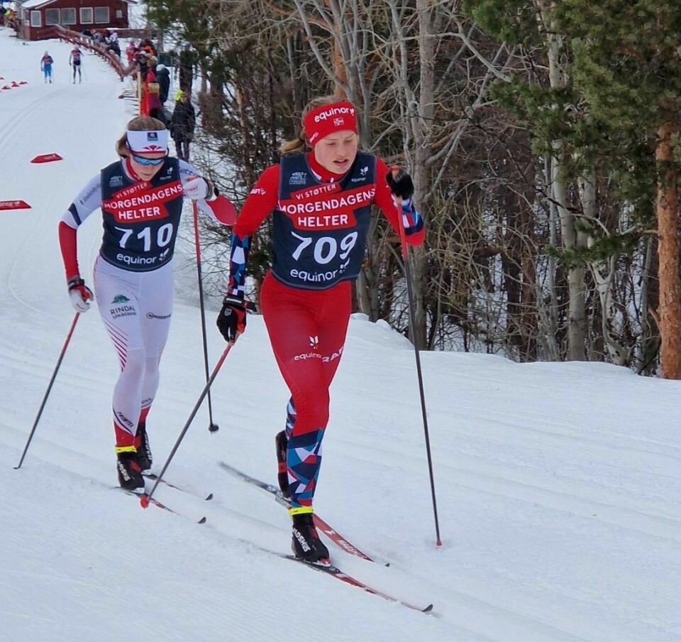 To jenter står på ski i oppover bakke. Fremst går en i rød drakt med startnummer 709 og bak går en med hvit drakt med startnummer 710.