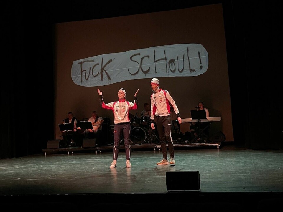 To ungdommer i Rindal IL-drakter står på scenen. Den ene med henden opp i lufta. Bak dem et lite orkester. På veggen bak dem står 'Fuck Schoul'.