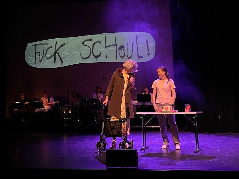 To ungdommer står på scenen og ser på hverandre. Den ene er normalt kledd og står bak et bord. Den andre er utkledd som eldre kvinne med grå parykk, gul kjole, brun kåpe og rullator. Bak dem et lite orkester. På veggen bak dem står 'Fuck Schoul' i spraymalt skrift.