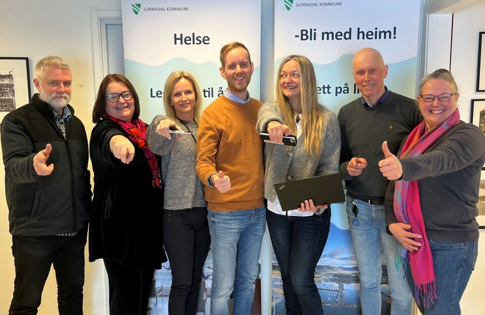 F.v: Assisterande rektor Surnadal barne- og ungdomsskule Bjørn Høivik, kommunalsjef samfunn Karin Halle, arkivleiar Sigrid Janne Moen, einingsleiar i teknisk drift Johan Kenneth Mogstad Åsenklint, rådgivar Anne Lise With Vullum, digitaliseringsansvarleg Pål Ranes og einingsleiar i heimetenesta Annett Ranes. Tre menn og fire kvinner som står ved siden av hverandre og peker mot kamera. Alle smiler. Bak dem er to roll-ups med slagord for Surnadal kommune.