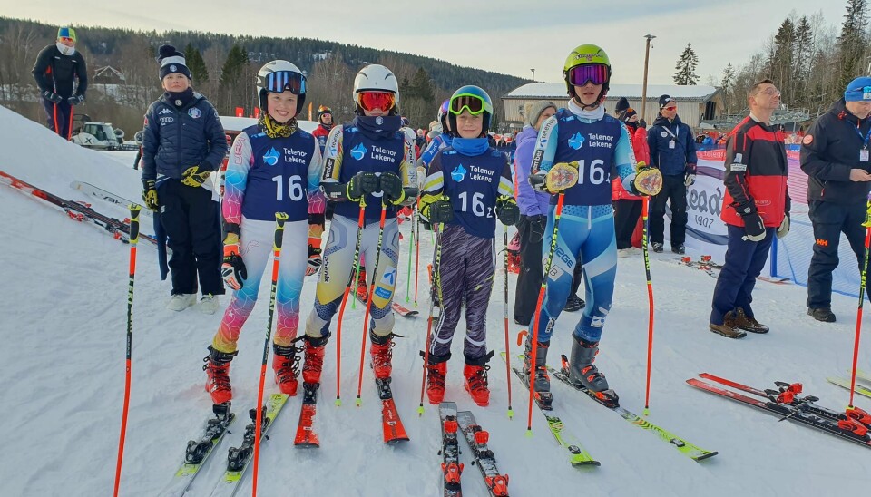 Fire barn/ungdom i alpinutstyr står ved siden av hverandre på en skiarena.
