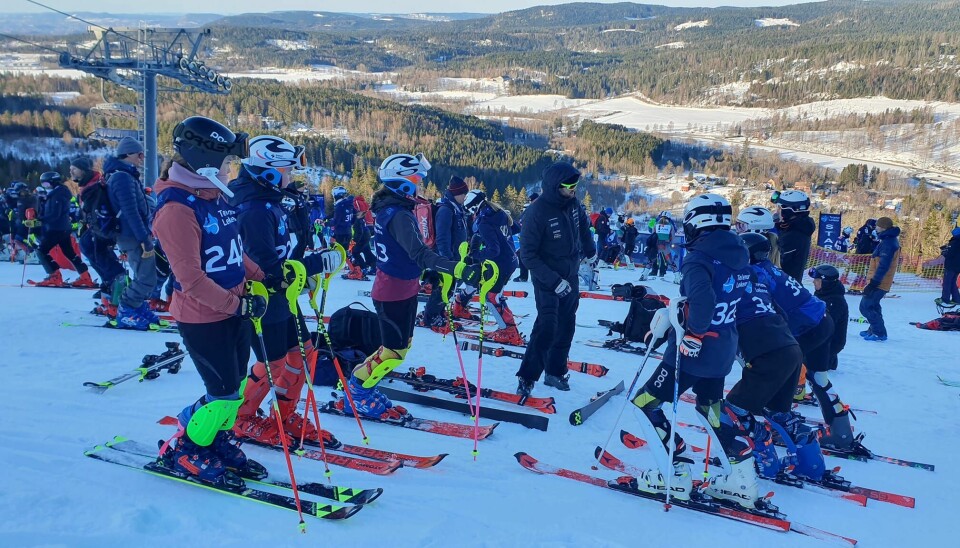Flere barn/ungdom i alpinutsyr står klare ved skiheisen på toppen av bakken.