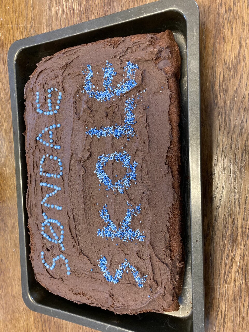 En sjokoladekake med blå strøssel hvor det står: Søndag Skole