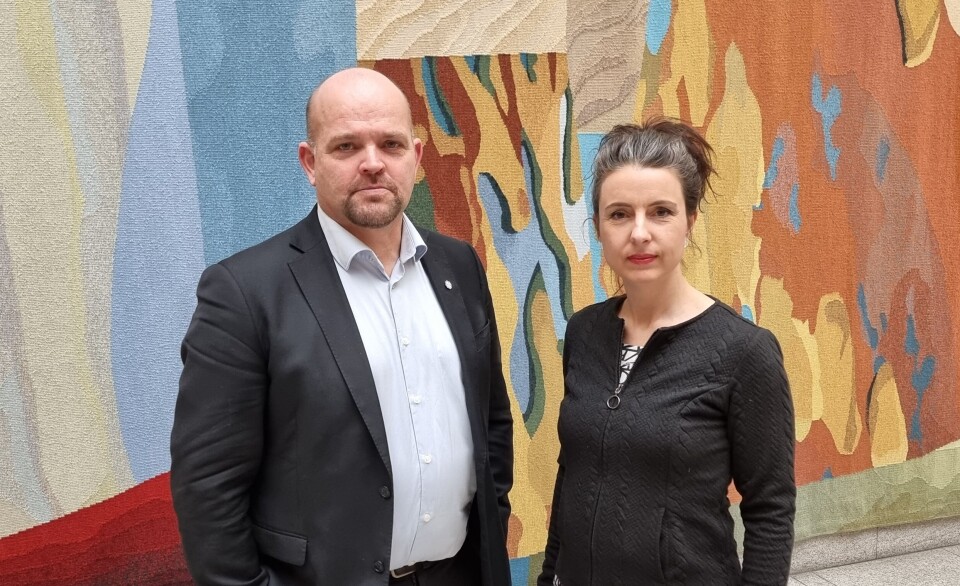 Geir Inge Lien og Jenny Klinge. En drasskledd mann og ei dame med langt oppsatt hår som står ved siden av hverandre og ser mot kamera med alvorlig mine. Bak dem en vegg med et stort vevd teppe i flere farger.