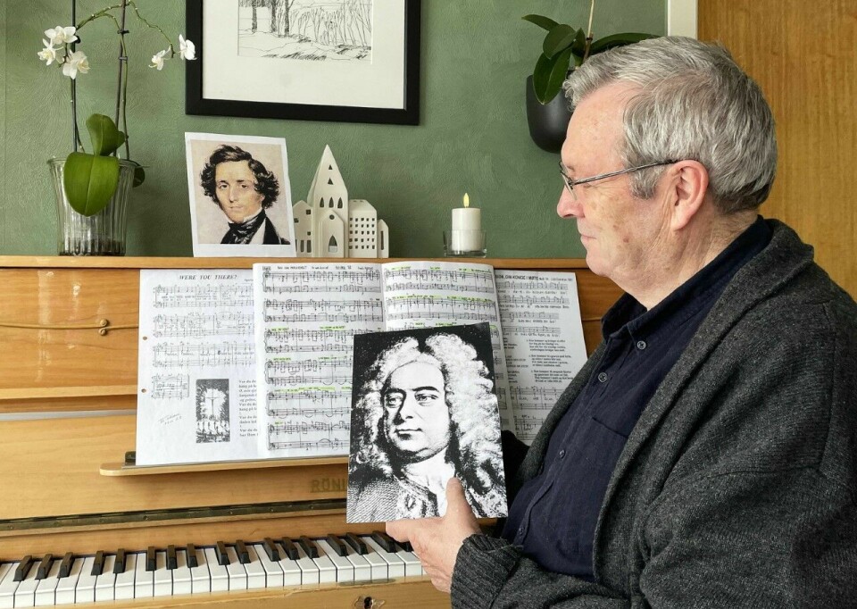 En mann sitter foran et piano med noter på og viser fram et bilde av en komponist.