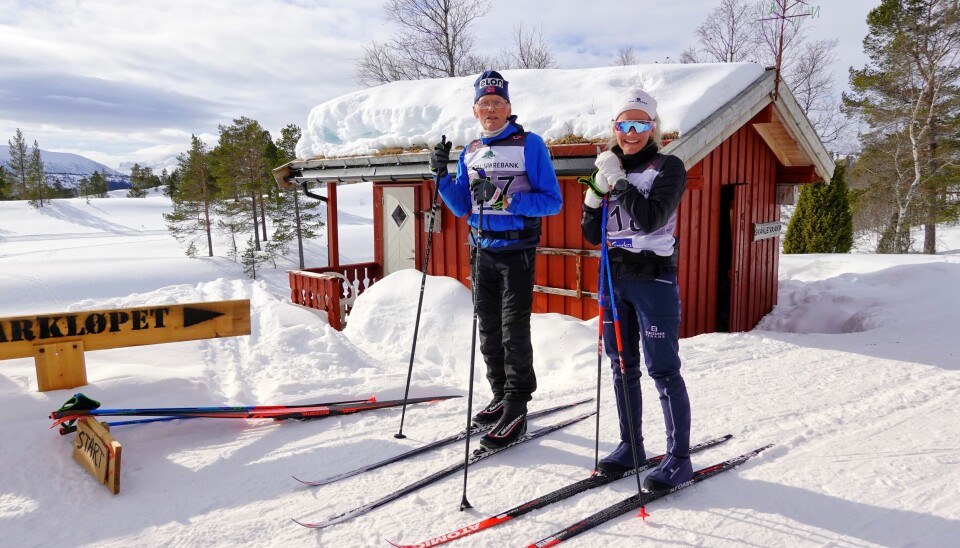 Bestefar med voksen barnebarn poserer stående på skia etter målgang