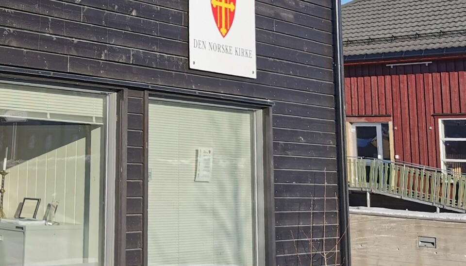 En utvendig vegg med et skilt med våpenskjoldet til den norske kirke, og tekst 'Den norske kirke'
