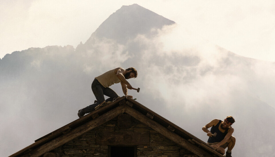To menn snekrer på et hustak med tåke bak seg og et høyt fjell i bakgrunnen