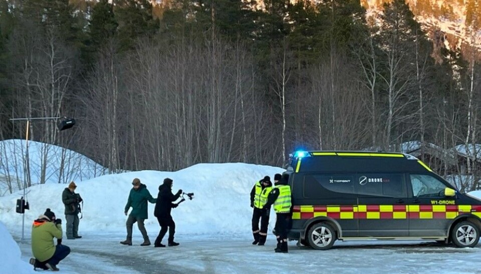 Et filmcrew står og filmer 3 mennesker i refleksvest foran en bil