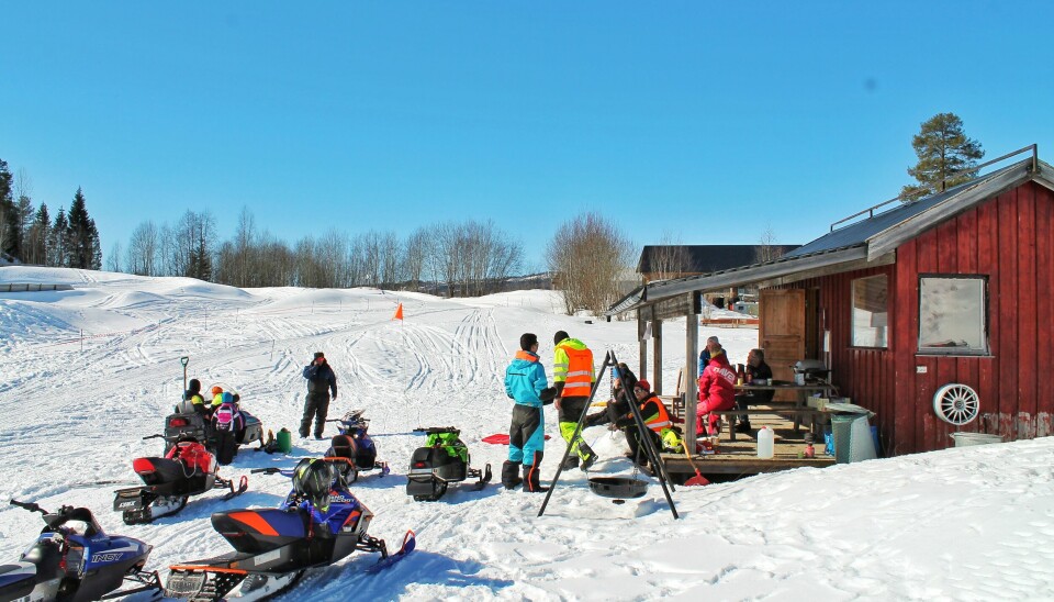 Mange snøscootere og mennesker ved et rødt hu står ute og griller