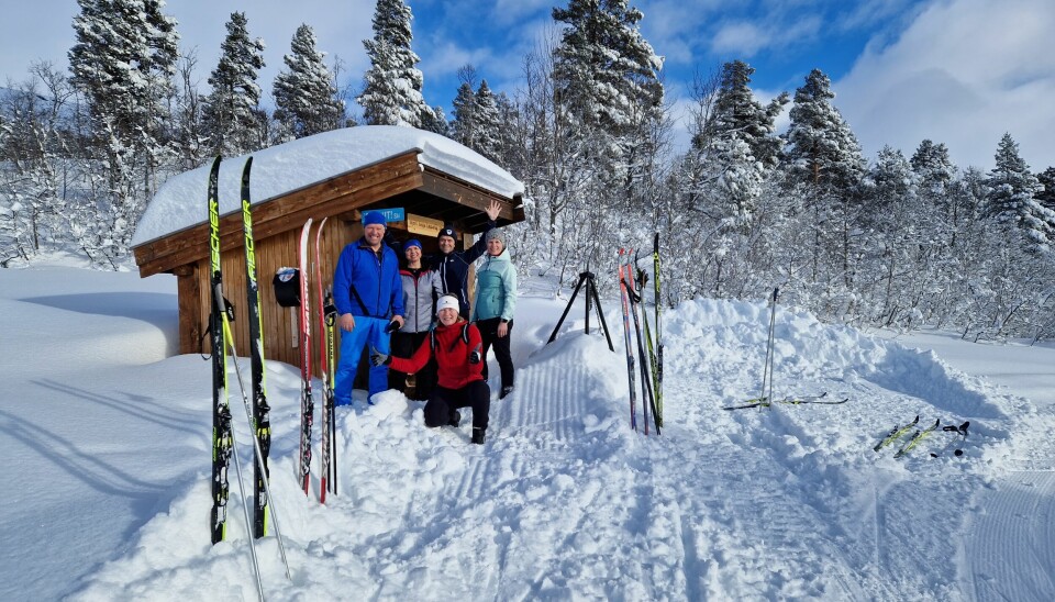 5 mennesker foran en gapahuk. Det er mye snø og ski står i snøen og ligger på bakken.