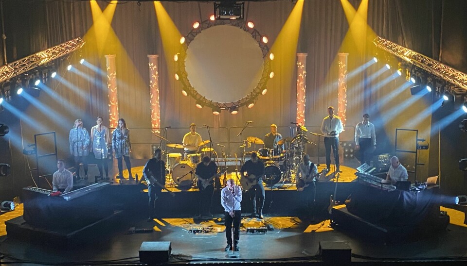 Et band på en scene og en vokalist står foran. Mye gult lysshow på scenen