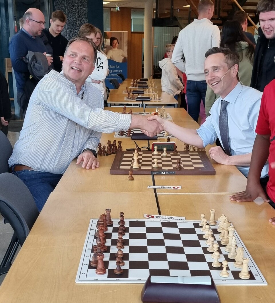 To menn tar hverandre i hånden over et sjakkbrett etter et slag med sjakk