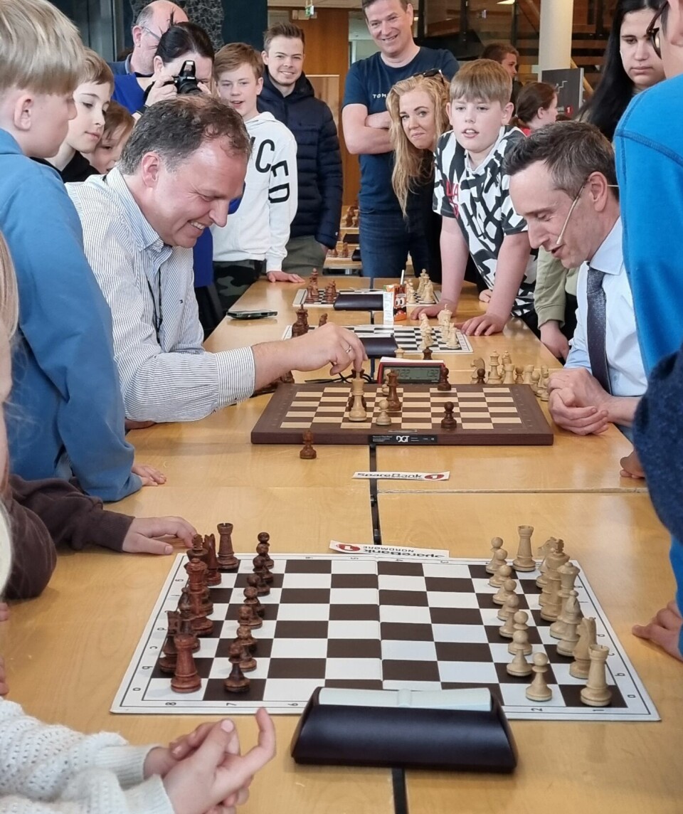 To menn spiller sjakk og mange barn og voksne står ivrig rundt og ser på.