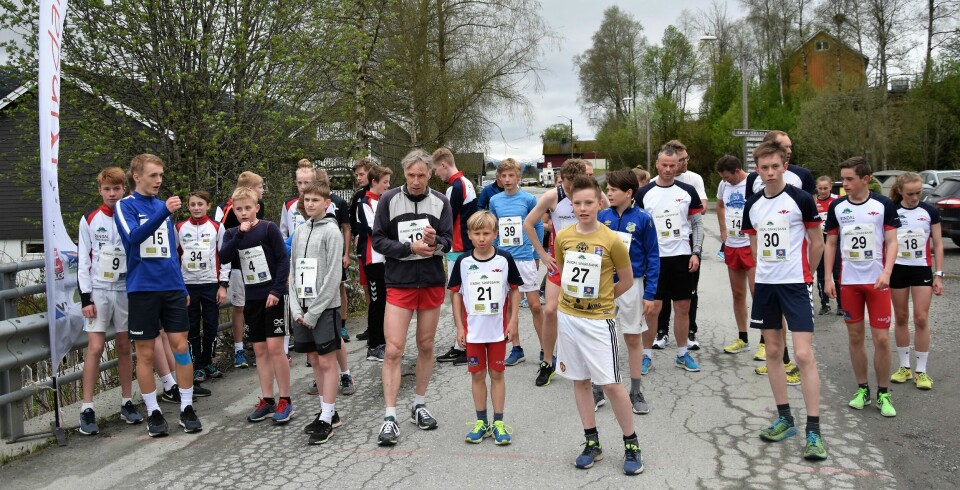 Mange barn og noen voksne med startnummer, klar for et utendørs løp.
