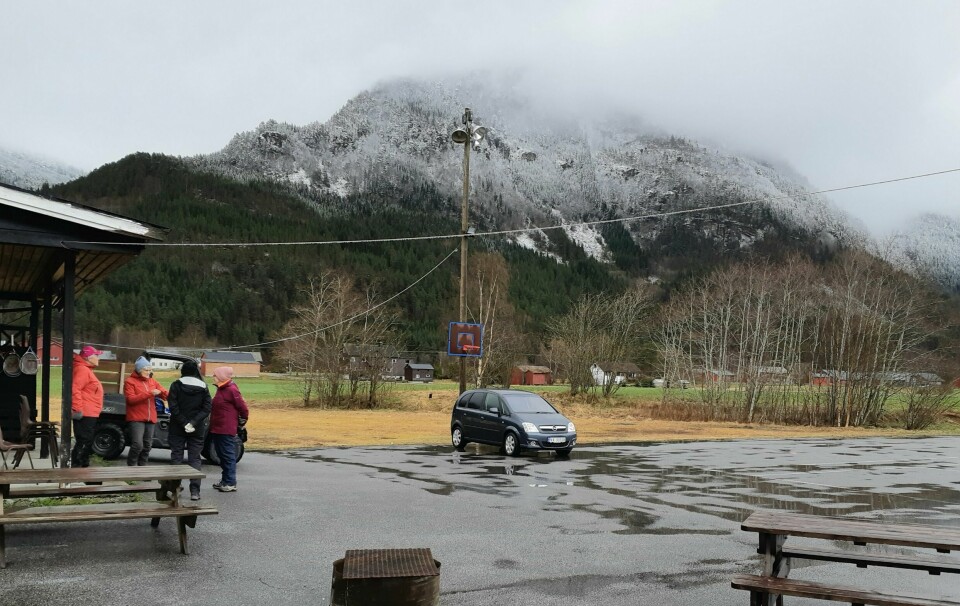 En parkeringsplass/rasteplass med en bil og noen mennesker. Regnvær. En snødekt fjelltopp med tåke i bakgrunnen.
