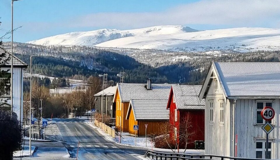 Gamle hus langs vegen i solskinn. I bakgrunnen er det snødekte fjell