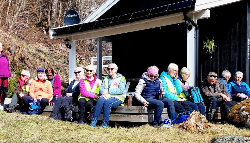 13 turkledde personer sitter utenfor ei hytte.