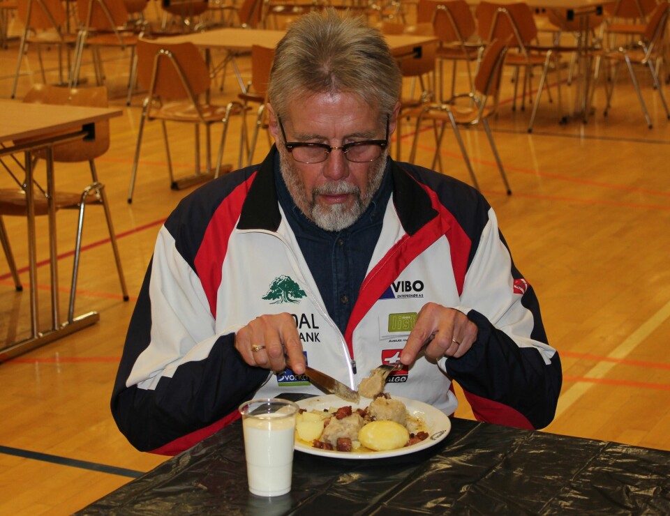 En mann med Rindal IL-jakke med en middagstallerken og et glass melk på borde foran seg.