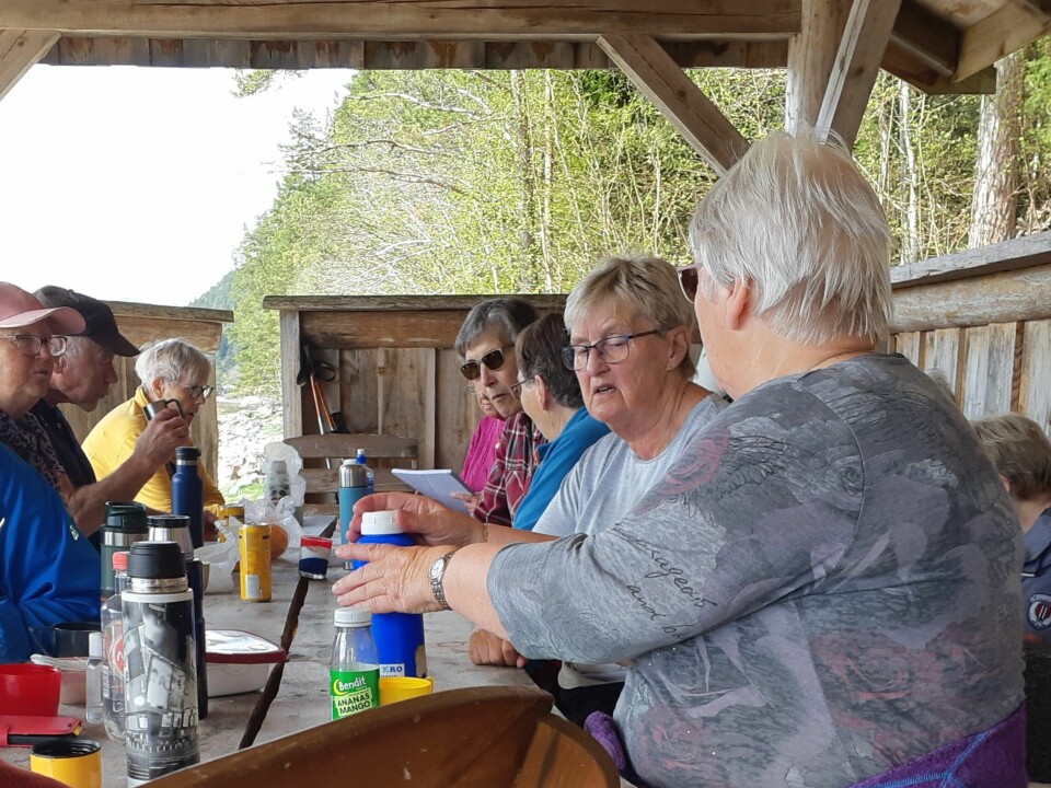En gruppe pensjonister på tur raster rundt et bord. Termoser og mat på bordet.