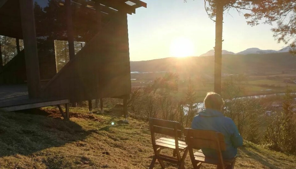 En person sitter med ryggen til kameraet og ser på solnedgangen bak fjellene