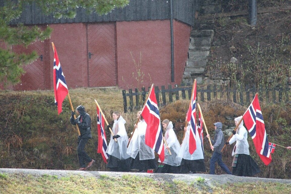 Barn går med norske flagg og regnponchoer