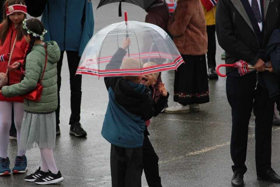 To barn smiler og ler under en paraply i regnet