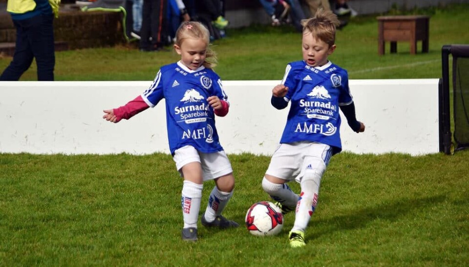 To barn i fotballdrakter med en ball på en fotballbane.