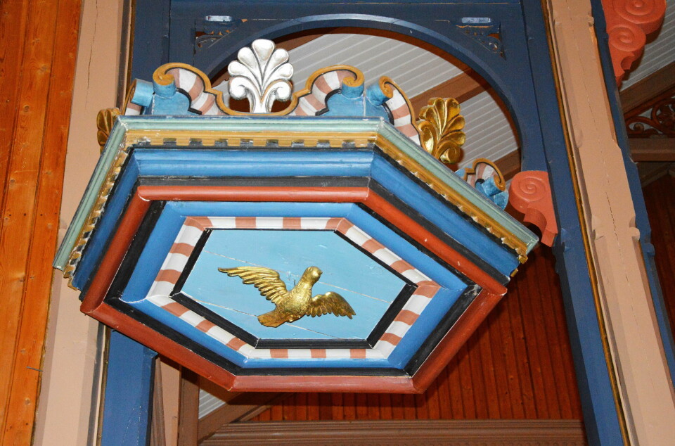 Utsmykning over prekestolen i ei kirke, med blant annet ei due i gull.