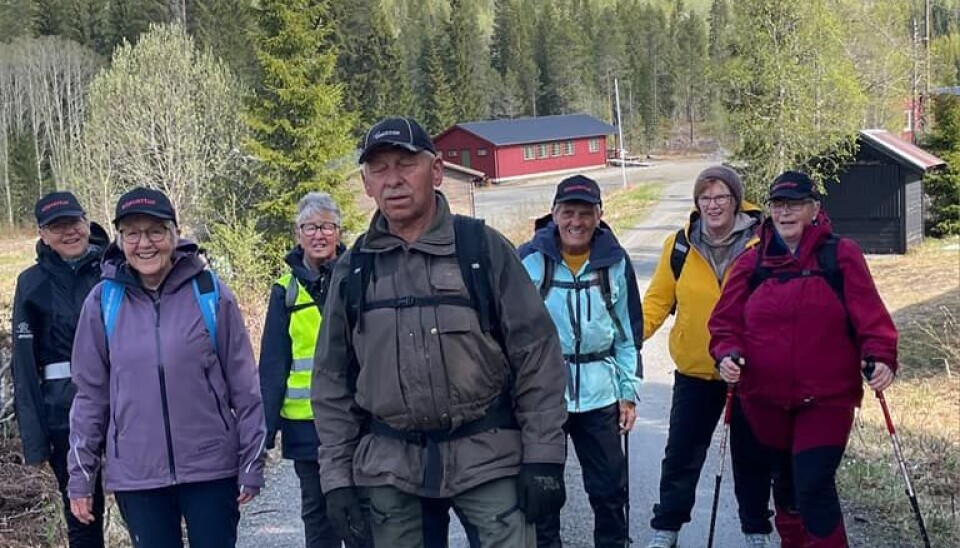 7 turkledde personer på en grusvei i en barskog. Noen hus i bakgrunnen.